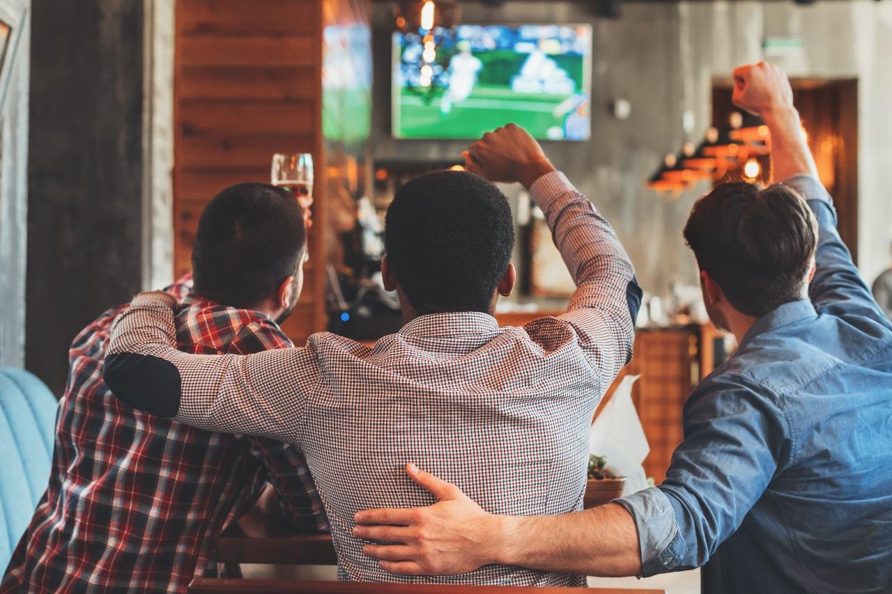 Grupo de amigos bebendo enquanto assistem a uma partida de futebol